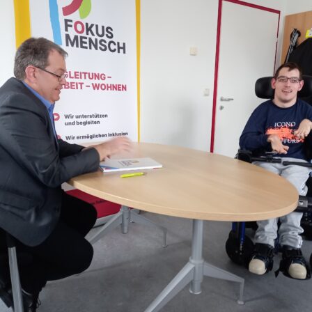Michael Leitner am Schreibtisch mit Alex Glatz, ein junger Mann im Rollstuhl